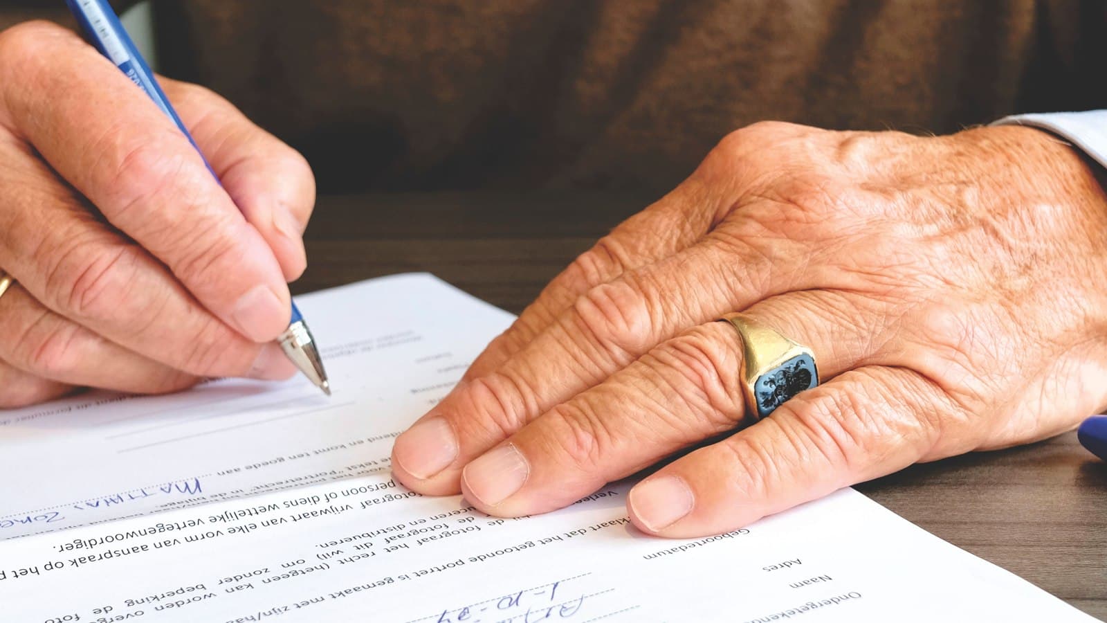 An older hand signing a document with a pen