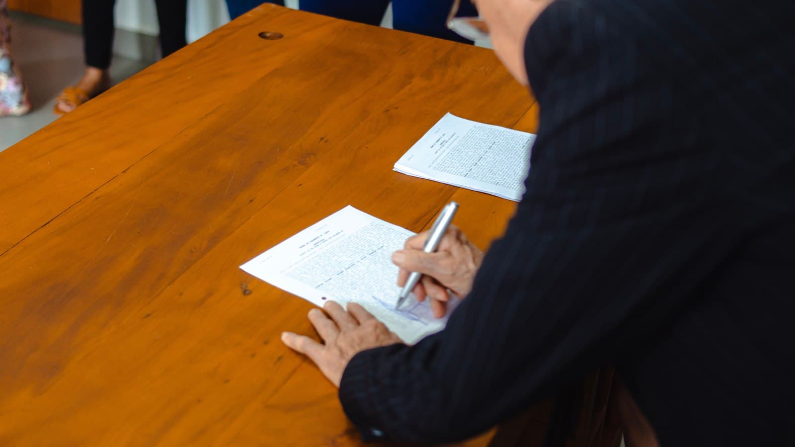 A person signing a form at a wooden desk