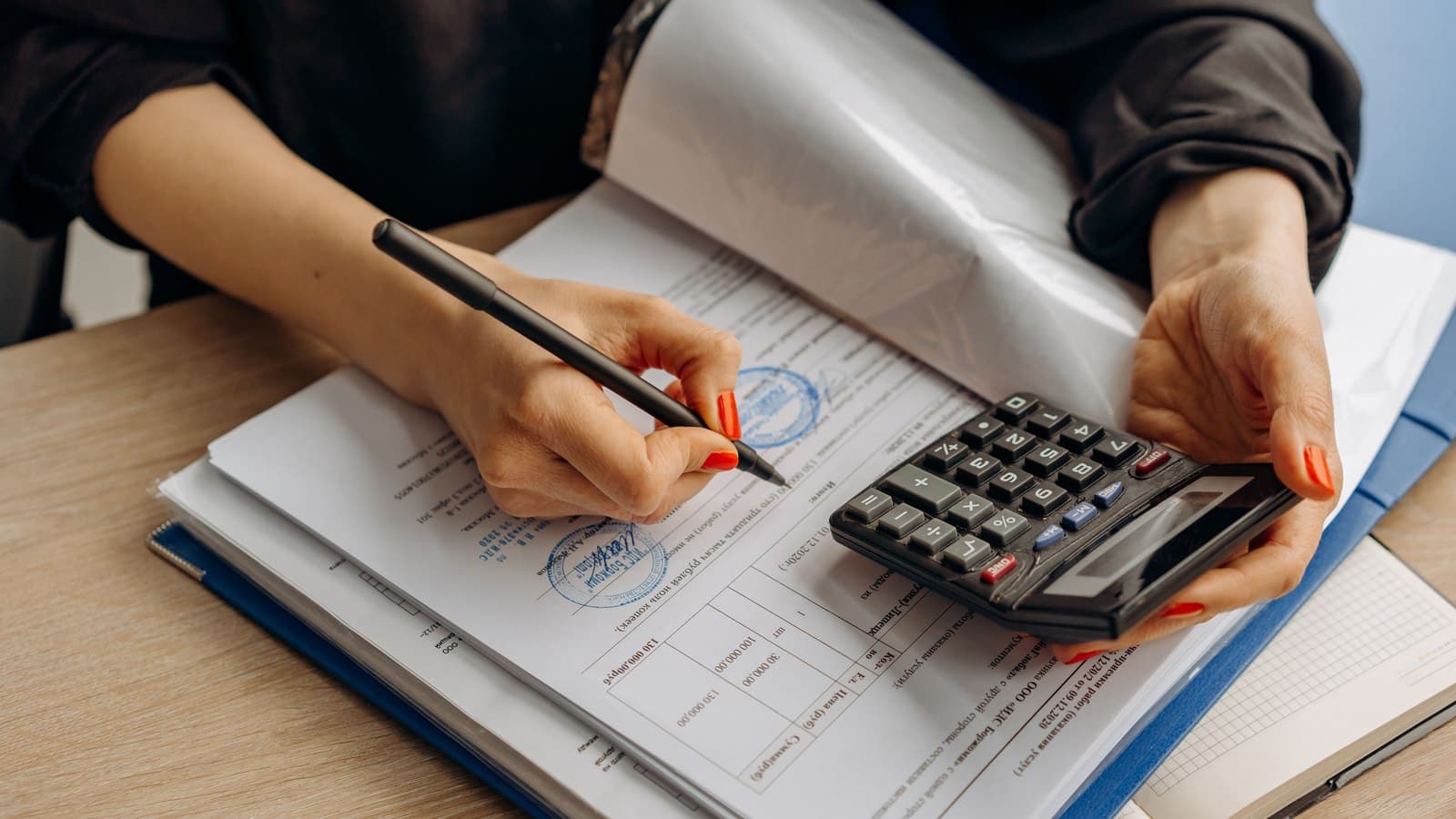 A person working through stamped forms with a pen and a calculator