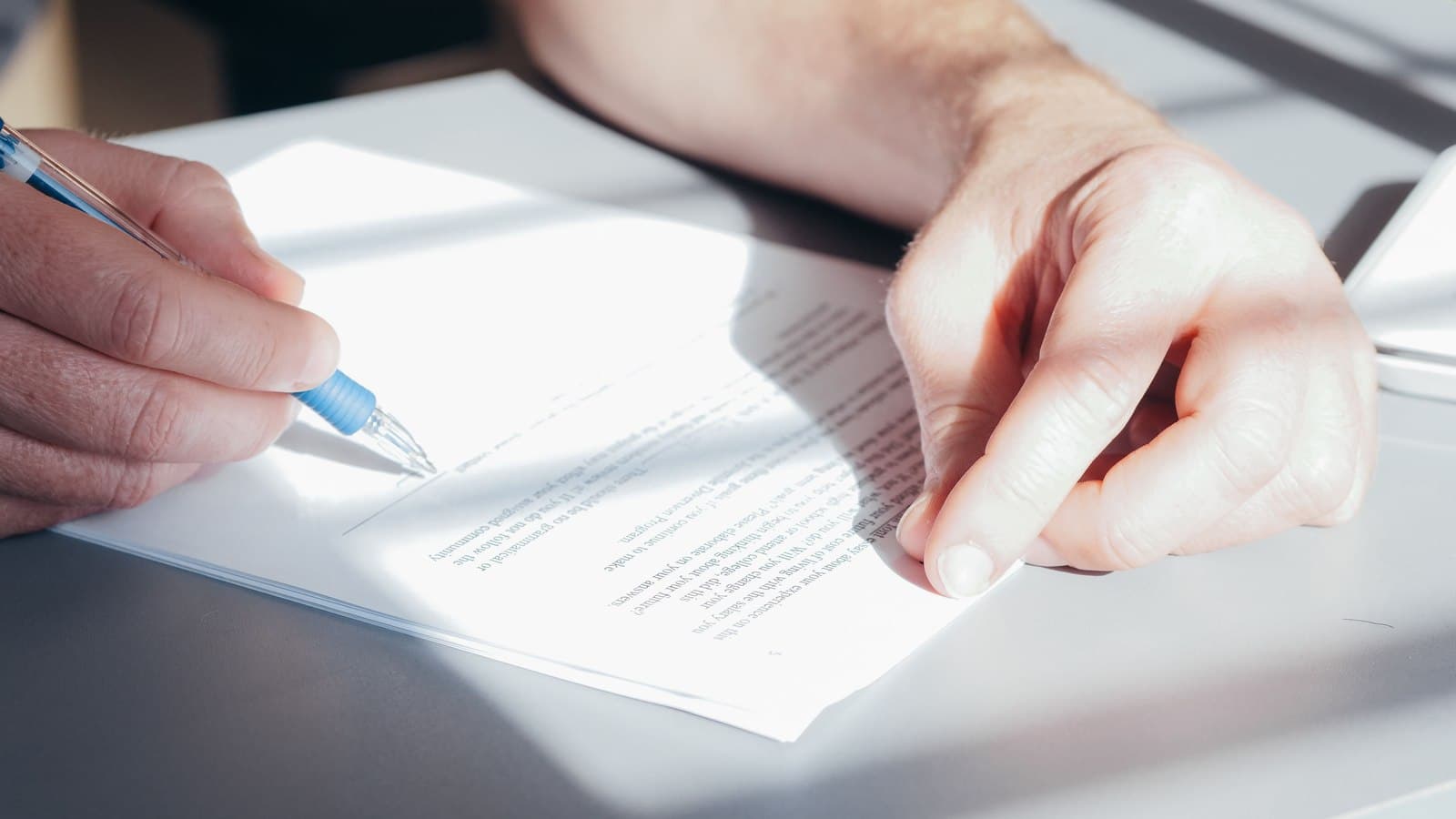 A hand signing an application form with a pen