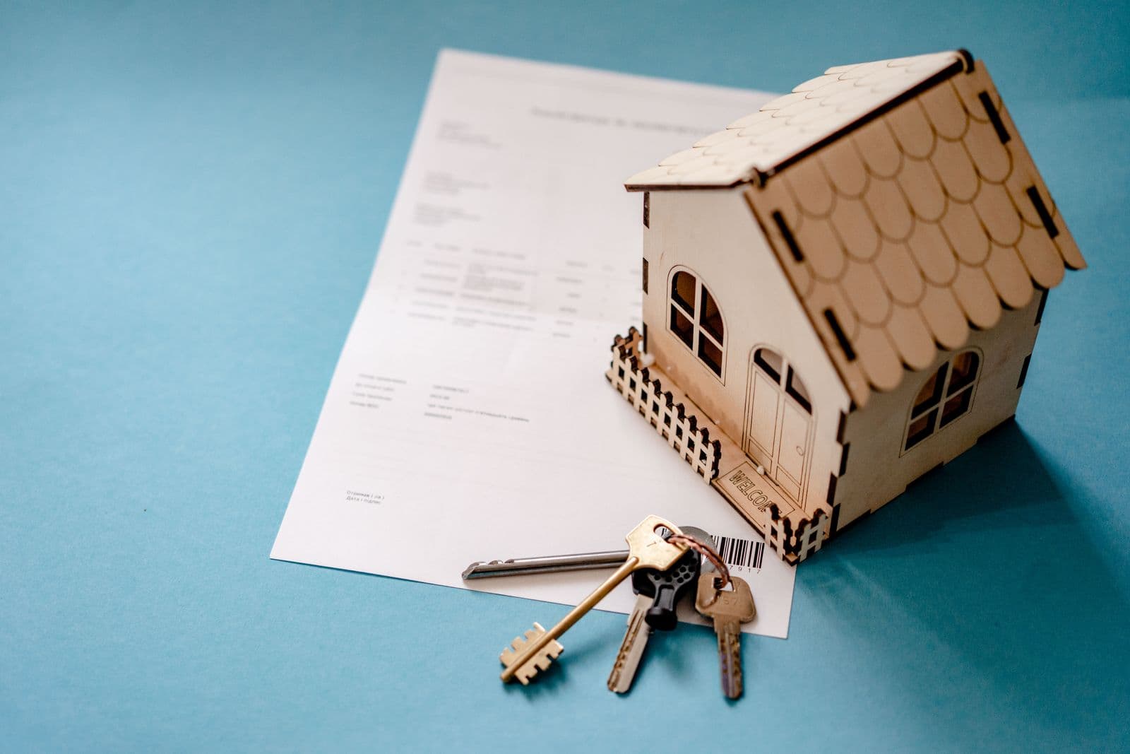 A small wooden house model beside a set of keys and a signed contract on a table