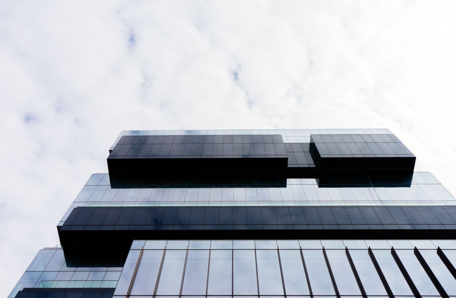 A glass office building facade with a repeating geometric pattern, seen from below