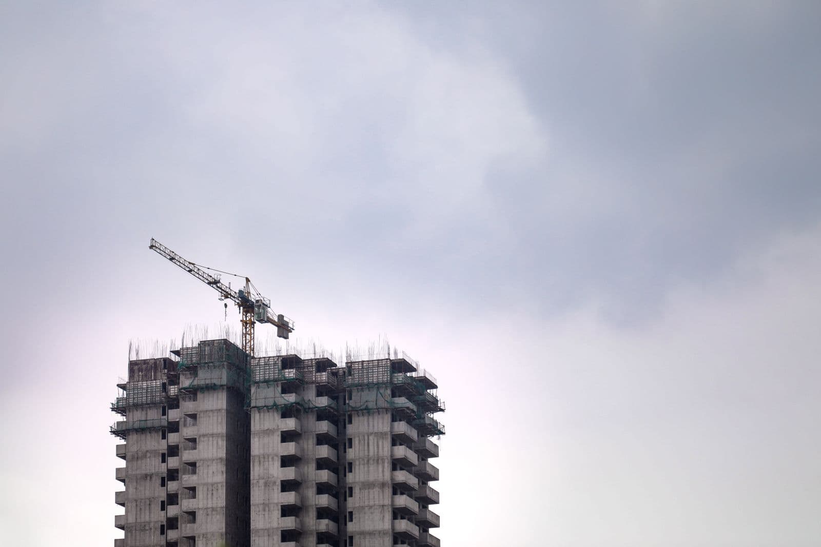 A high rise concrete building under construction with a tower crane against a cloudy sky