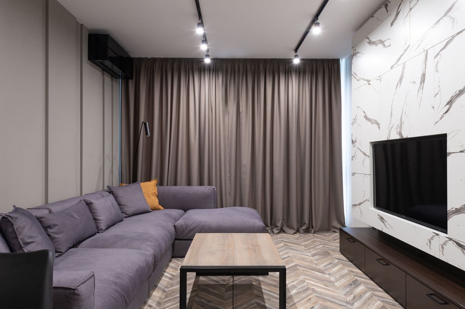 A living room with a deep sofa, full height curtains and a marble media wall