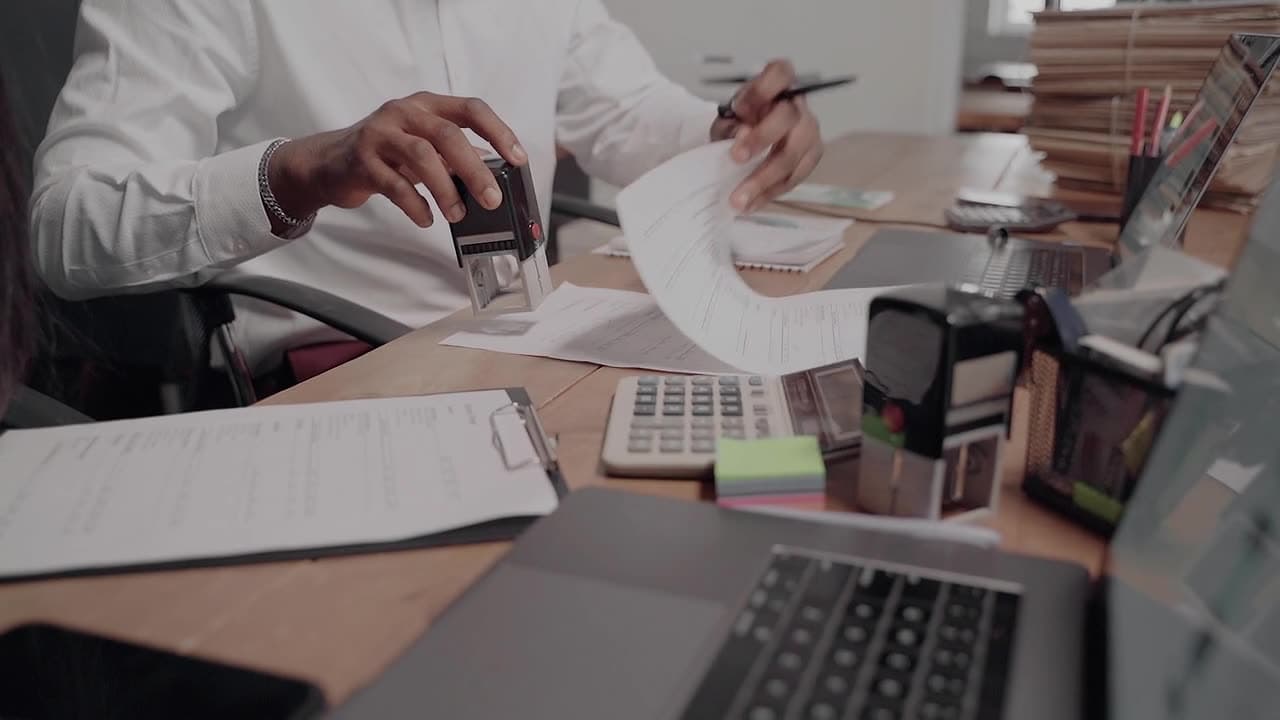 A hand pressing a rubber stamp onto an application form on a desk