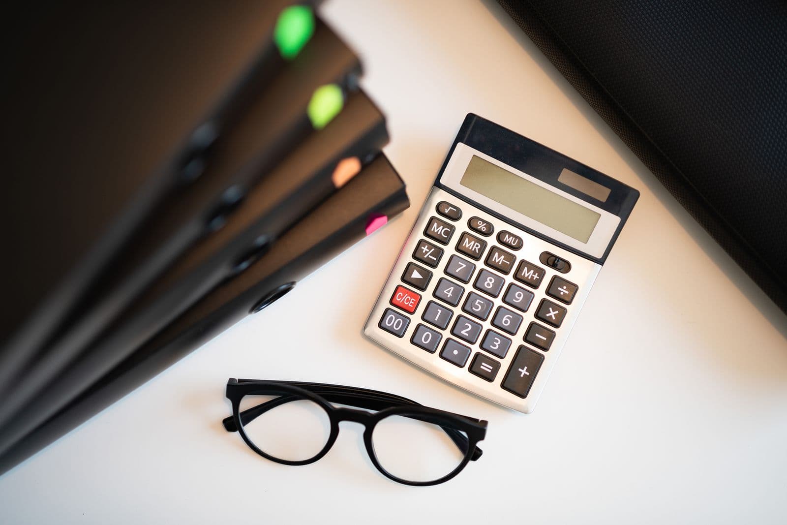 A desk with files, a calculator and a pair of glasses